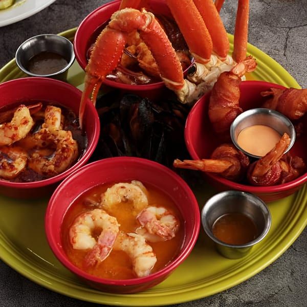 A vibrant platter of Mexican seafood, including crab legs, shrimp in red sauce, and bacon-wrapped shrimp.