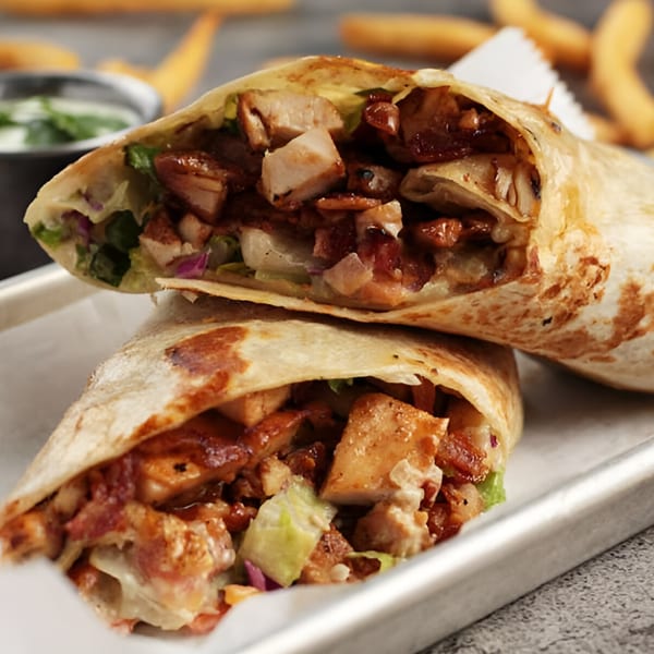 Two halves of a chicken burrito, filled with meat, lettuce, and red onion, on a metal tray.