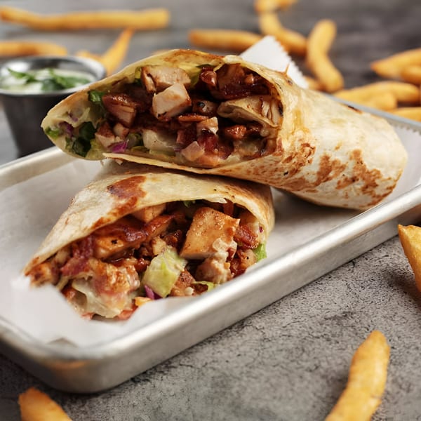 Two halves of a chicken burrito with sauce and vegetables, served with fries and dip.