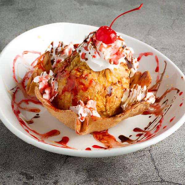 Fried ice cream dessert in a taco shell bowl, topped with whipped cream, cherry, and sauces.