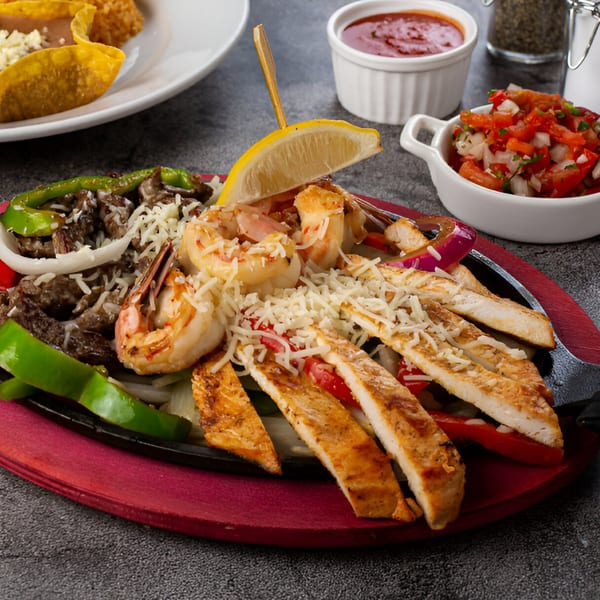 Sizzling fajitas with chicken, steak, and shrimp, topped with cheese and a lemon wedge.